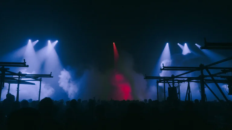 Eine große Menschenmenge feiert in der Jahrhunderthalle Bochum mit Lichtstrahlen, Nebel und Gerüststruktur.