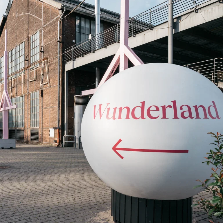 Eine große weiße Kugel mit der Aufschrift "Wunderland" und einem Pfeil deutet den Weg zum Festivalzentrum der Ruhrtriennale, vorbei an der Jahrhunderthalle Bochum.